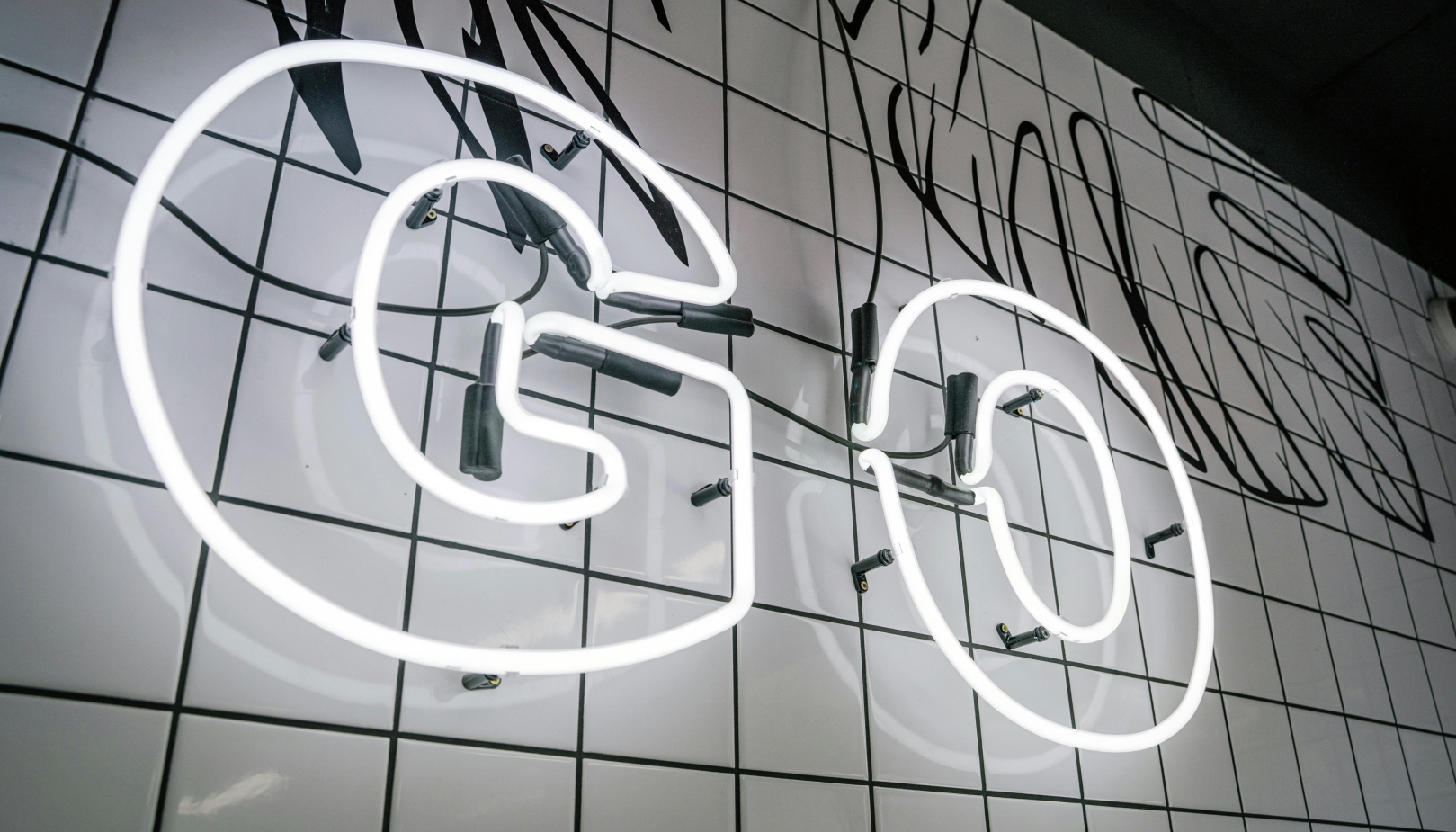 White neon sign spelling "GO" mounted on a tiled wall with black wire supports.