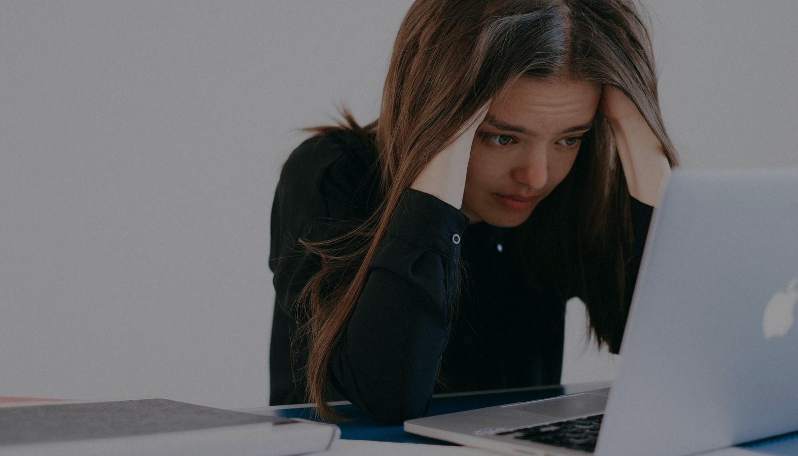 Young woman in a black shirt holding her head in frustration while looking at a laptop screen.