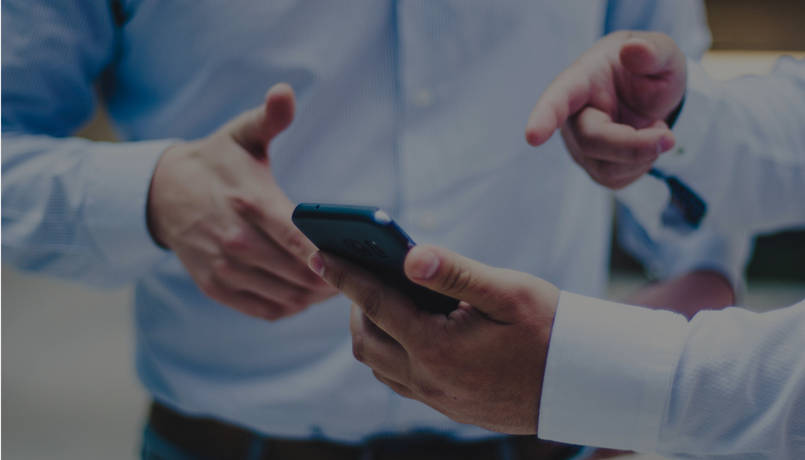 Close-up of two business professionals in white shirts discussing something while holding a smartphone.