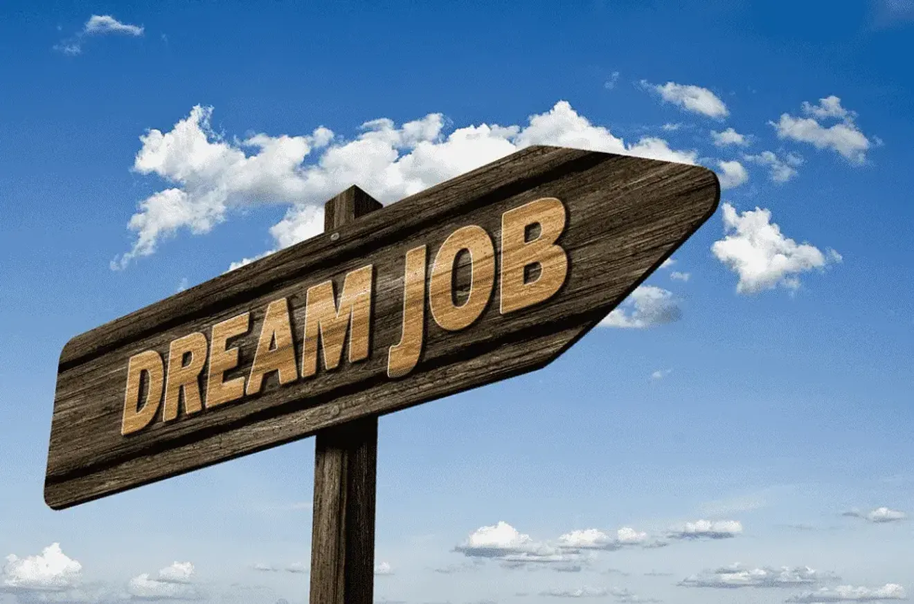 Wooden signpost reading “Dream Job” pointing toward a bright blue sky, symbolizing career aspirations and opportunities
