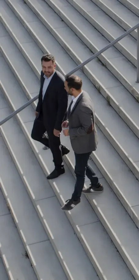 Two men in suits ascending a staircase, engaged in conversation as they move upward Two men in suits ascending a staircase, engaged in conversation as they move upward