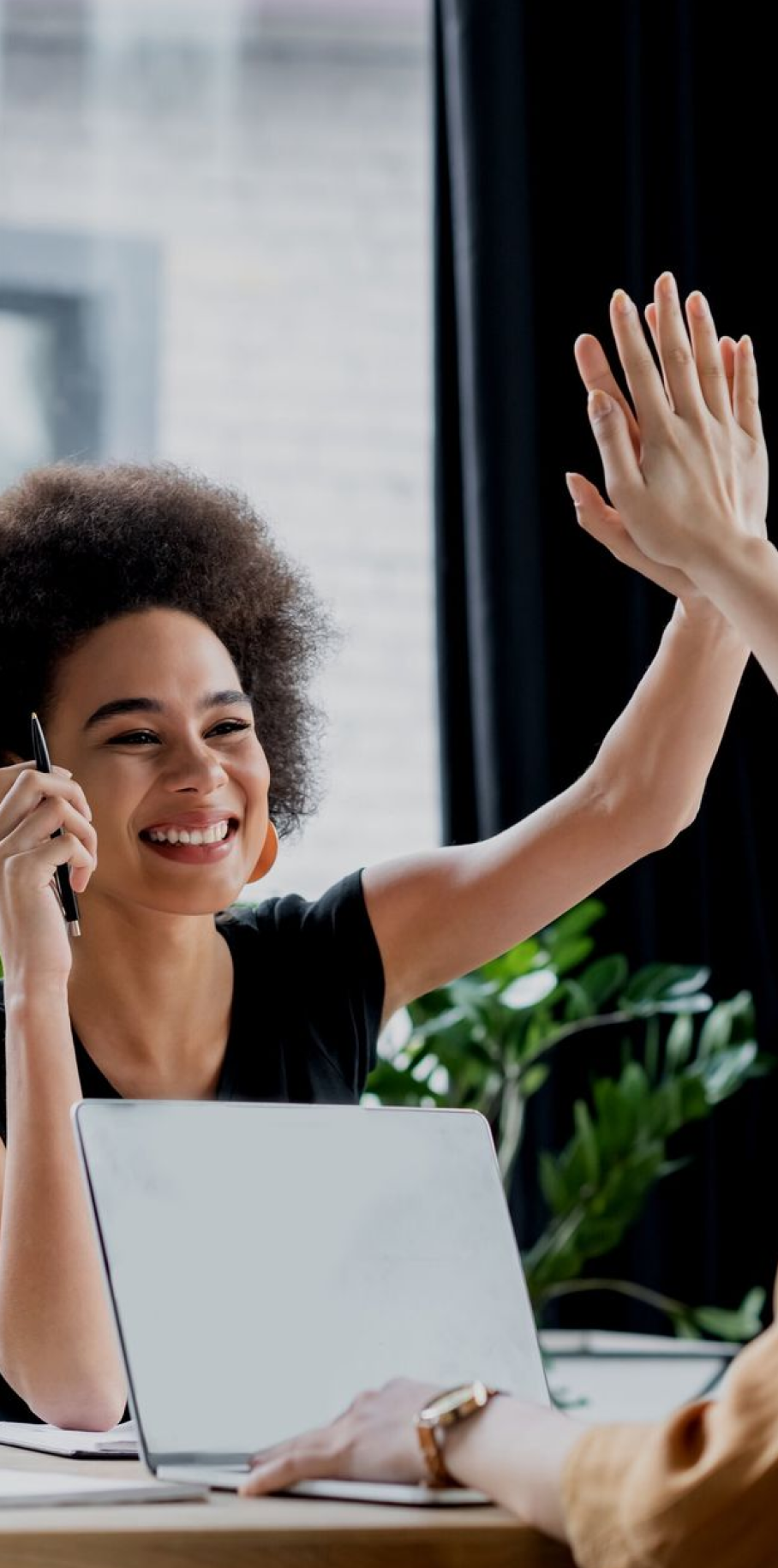 Two women enthusiastically high five each other while seated at a table, celebrating a shared moment of joy